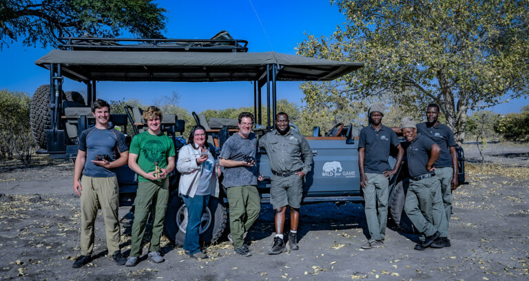 Safari guide team and guests standing beside open 4x4 safari vehicle in Botswana