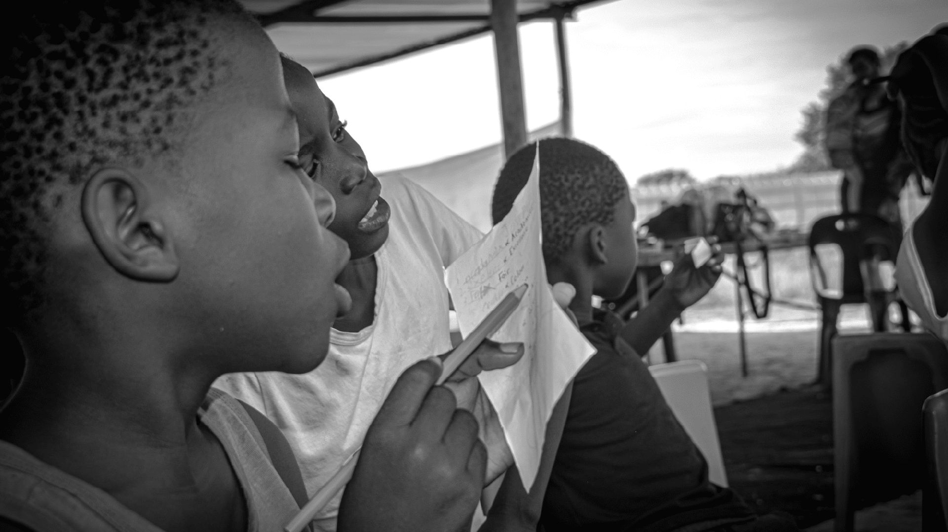 Our partnership wiht lehikenf for the developmnent of children wild for game group of children seated outdoors reading papers together during a shaded activity wild for game